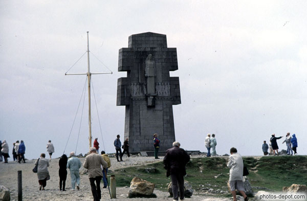 Statue de femme sur monument en croix et mat de bateau à voile