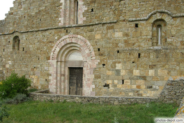 photo de Facade Ouest typique de l'art roman du XIIe en pierre granitique. Portail de marbre rose de Villefranche de 3 teintes pour les linteau, tympan et et voussures. Archivolte soulignée d'un bandeau de dents d'engrenage