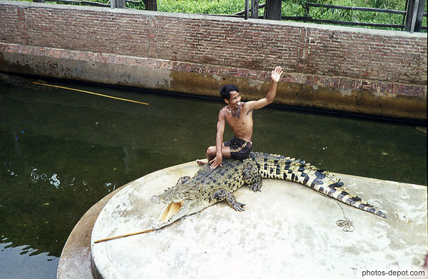 photo d'homme salue, assis sur un superbe crocodile caiman gueule ouverte