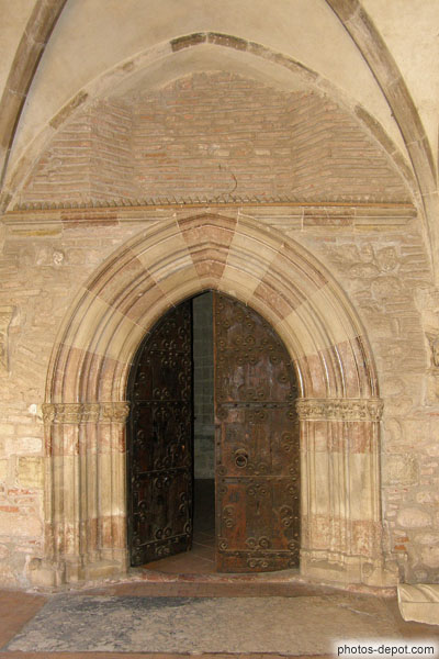photo de Portail gothique de marbre blanc et rouge alternés, porte décorée de pentures romanes de fer forgé menant à l'abbaye