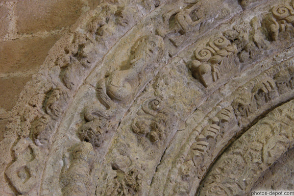 photo d'archivoltes supérieures du portail : des têtes plates, des monstres fantastiques, serpens à tête d'homme